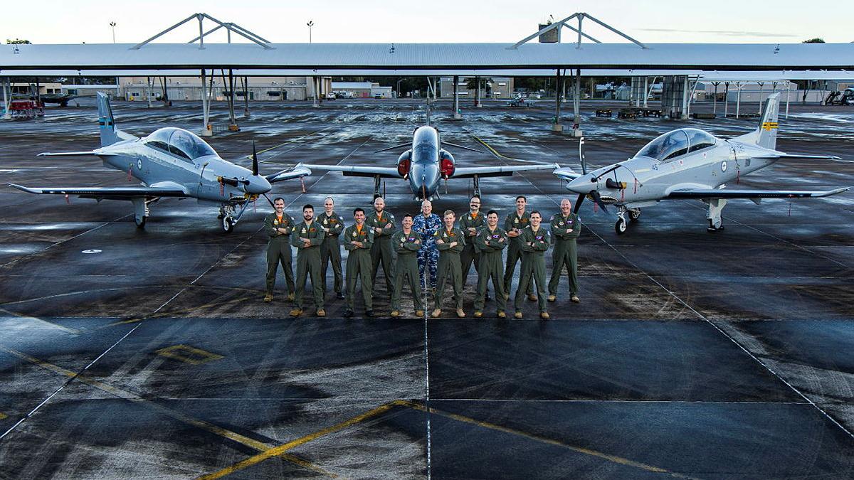 Group photo of United States Test Pilot School students and instructors with Aircraft Research and Development Unit (ARDU) personnel with three parked aircraft at RAAF Base Williamtown, NSW.