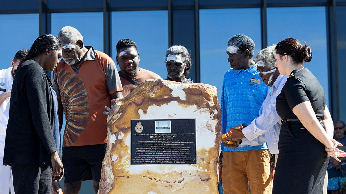 A group of people standing around a large rock with a memorial plaque on it.