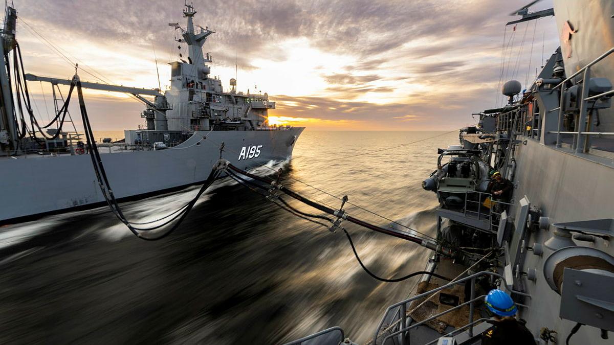 Two ships are connected by fuel lines while sailing together.