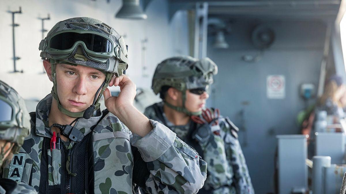 A sailor fixes his head gear on a ship.