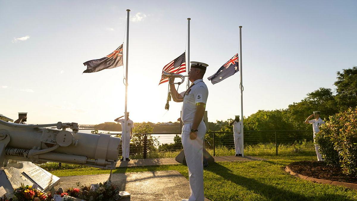 A sailor plays an instrument in front of national flags. 