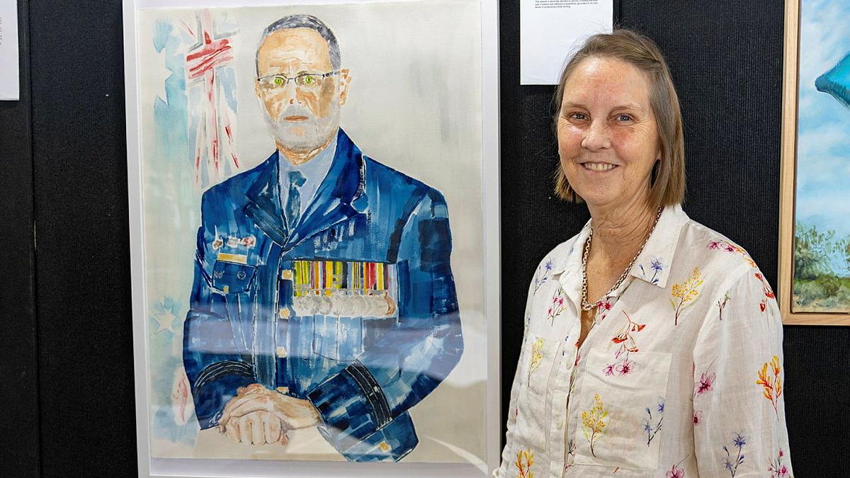 Royal Australian Air Force aviator Flight Sergeant Karen Tate-Smith stands with her portrait 'Devotion to Duty' at the 2026 Defending the Arts exhibition at the Australian Defence Force Academy.
