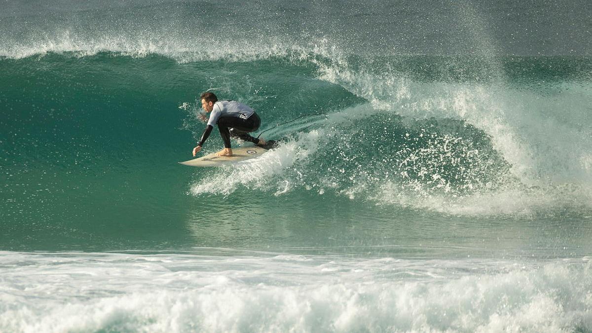 A male surfer rides an aqua blue waves with lots of spray coming off it.