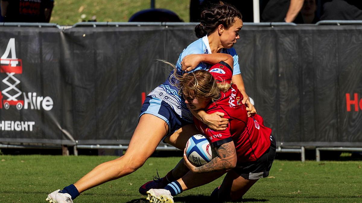A female rugby player tackles another female rugby player during a game.