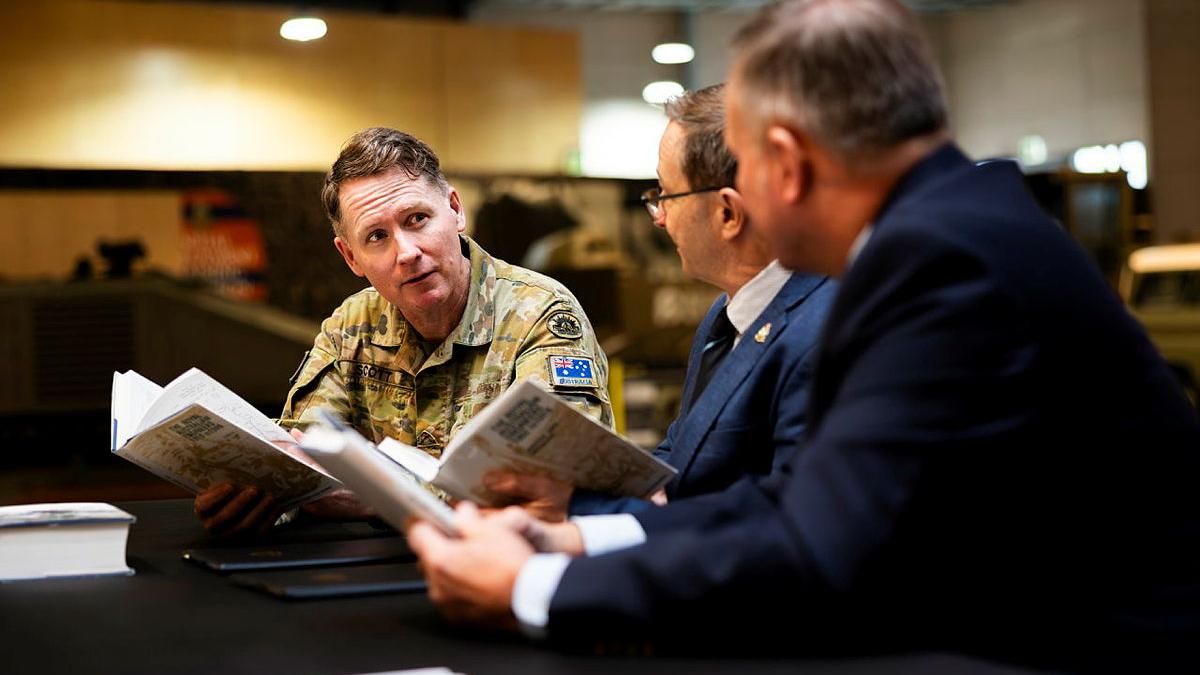 Three men sit at a table, each holding a book.