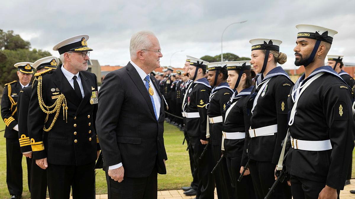 Navy personnel stand in line as they are inspected by two officials.