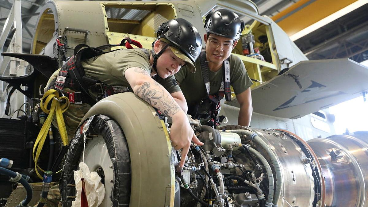Two people work on servicing a military helicopter.