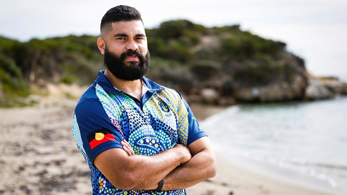A man stands on the beach with his arms crossed.