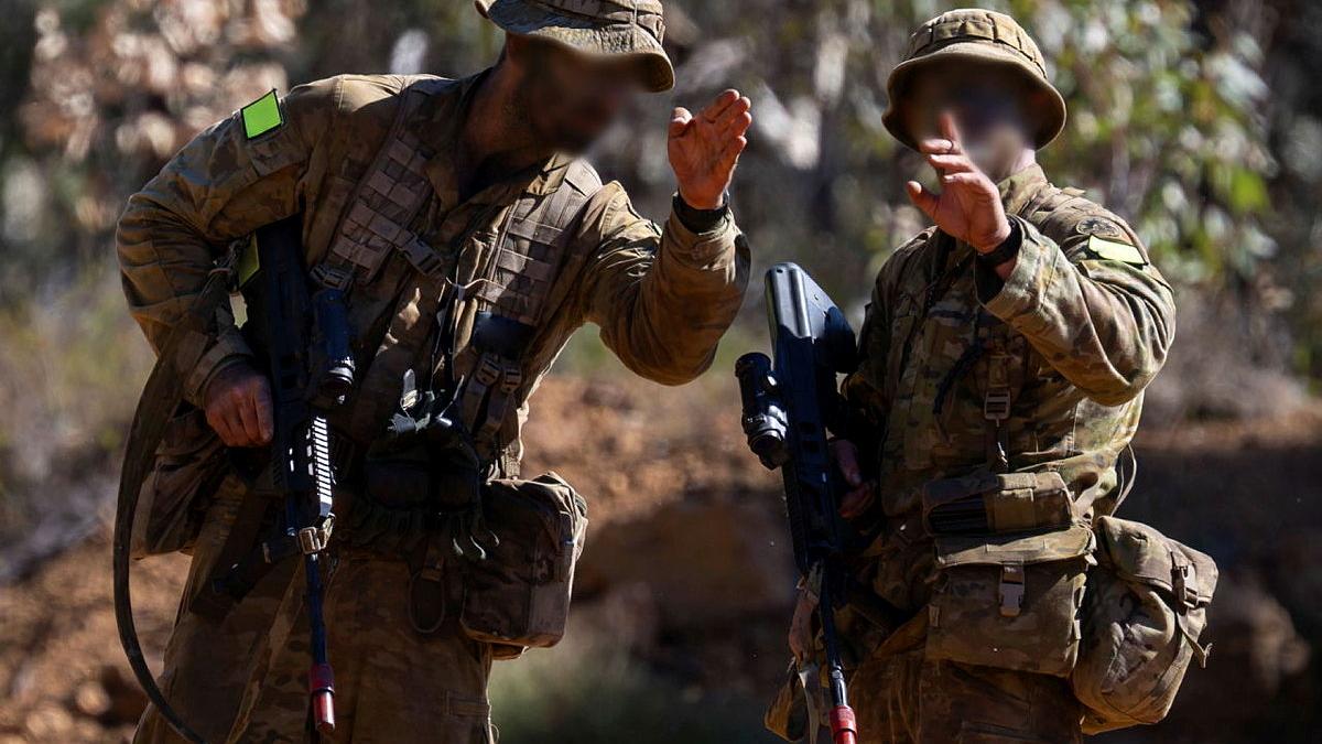 Two Army members in full uniform direct with hand signals.
