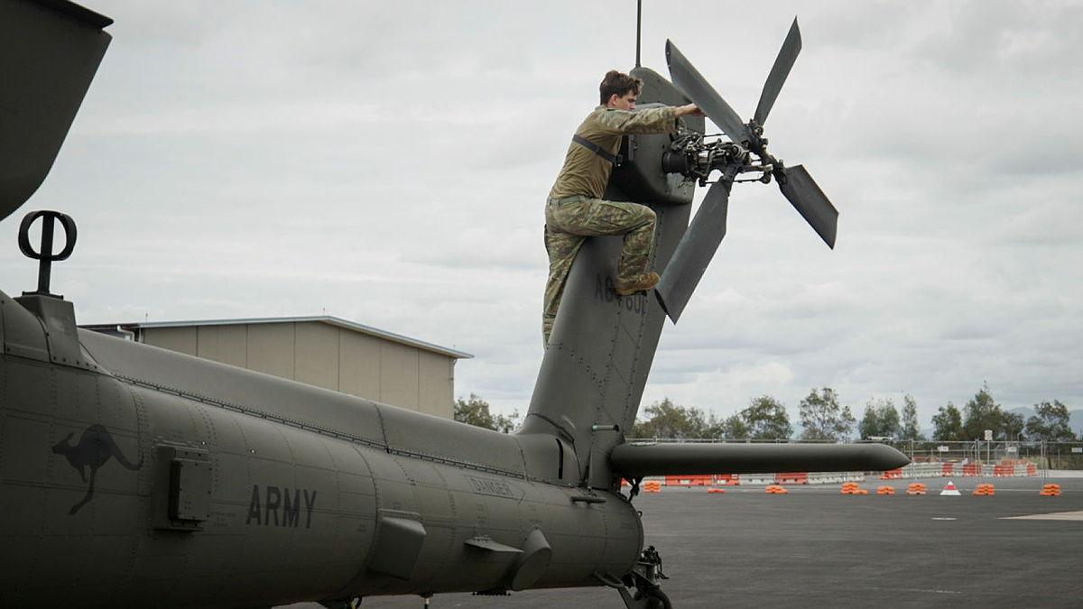 An Army pilot climbs up the tail of a helicopter on the tarmac.