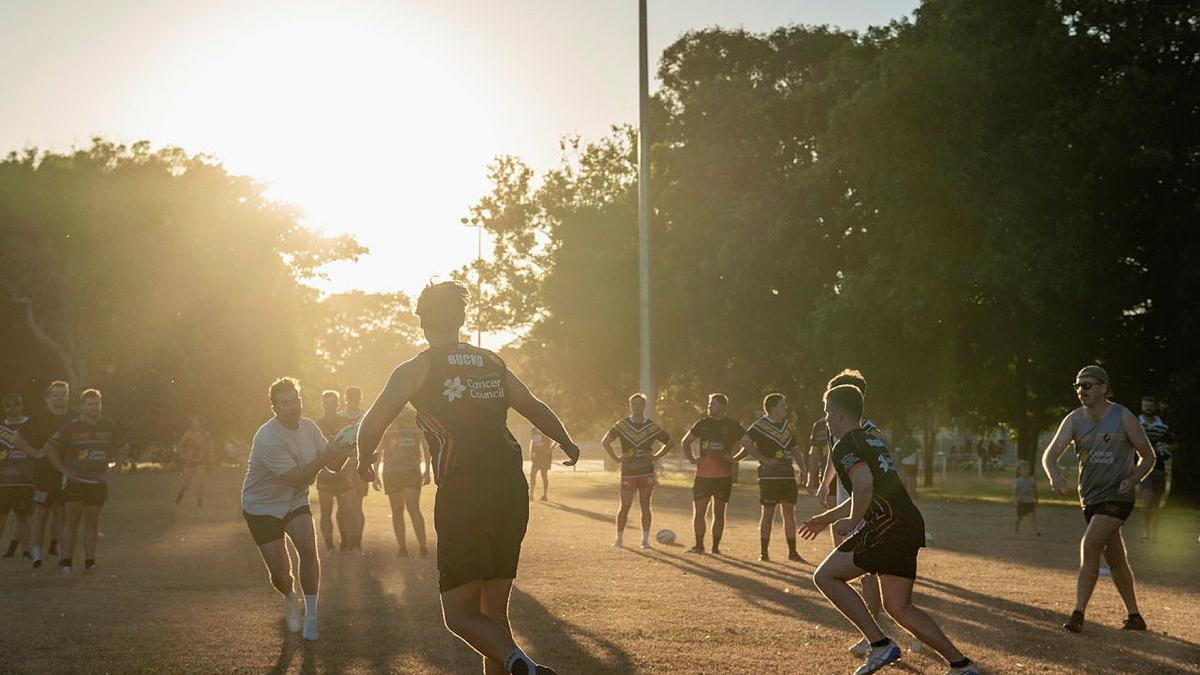 People playing rugby outside as the sun sets.