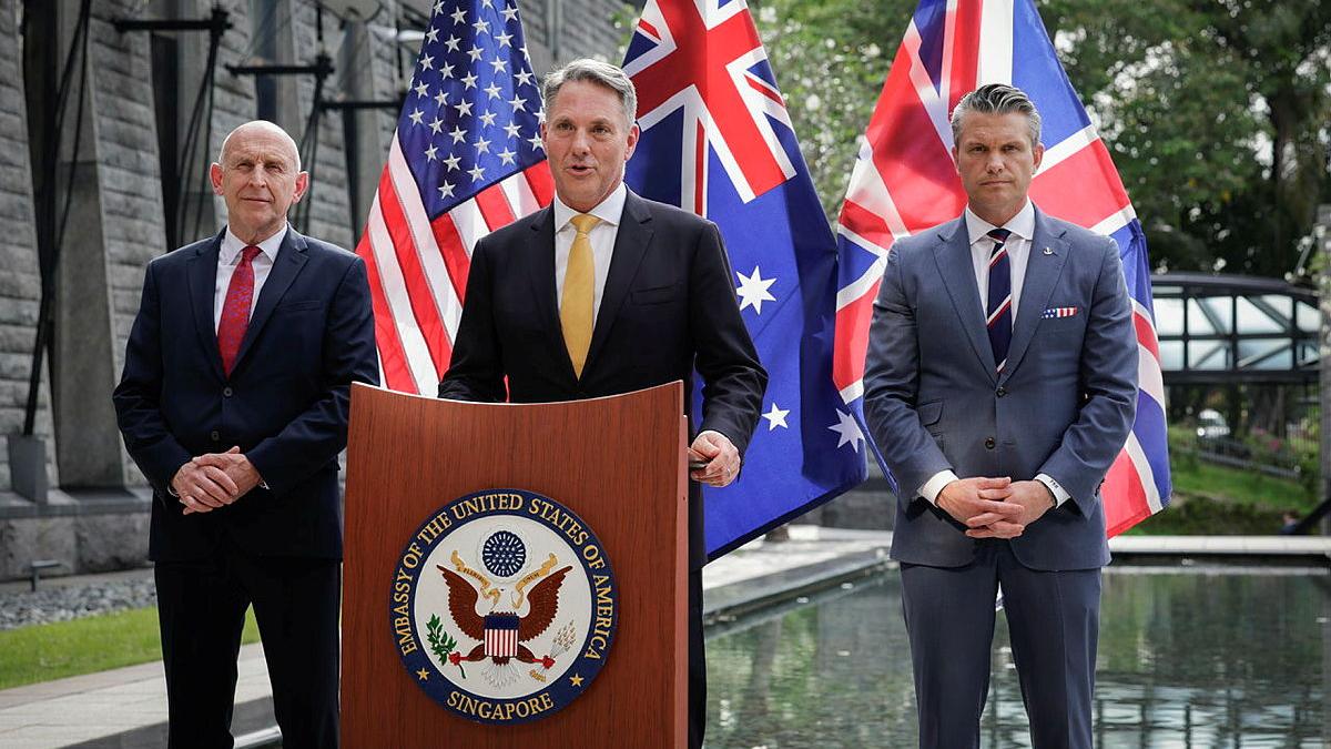Three men in suits stand in front of US, Australian and UK flags.