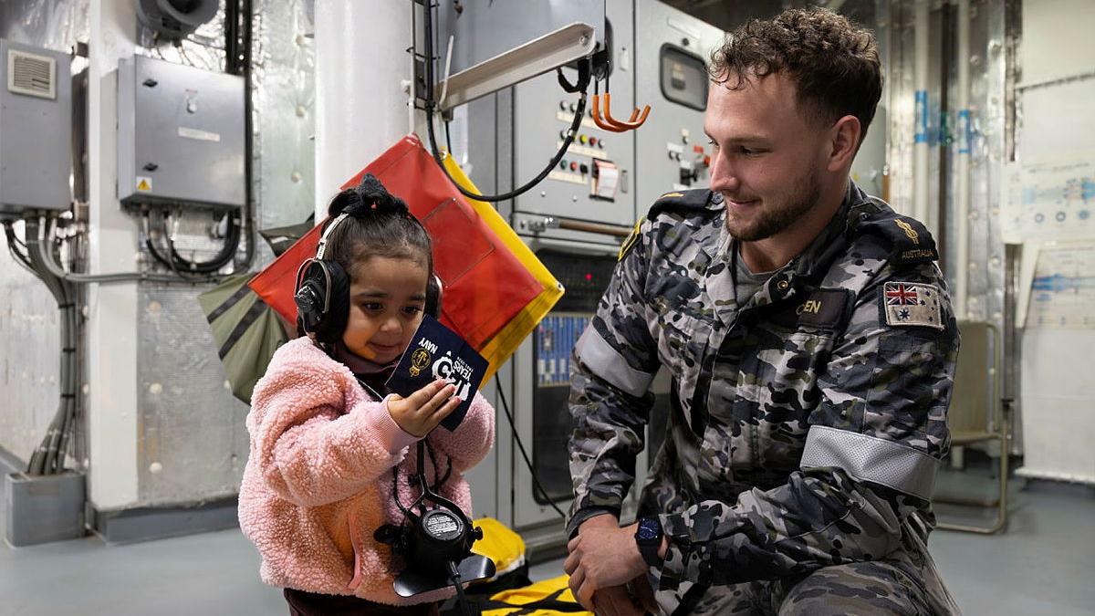 A sailor shows equipment to a child wearing headphones.
