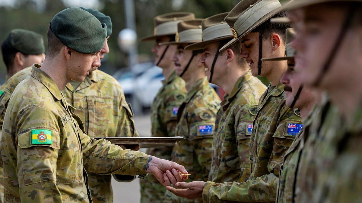 Army trainees standing in a line receiving badges from another Army member.