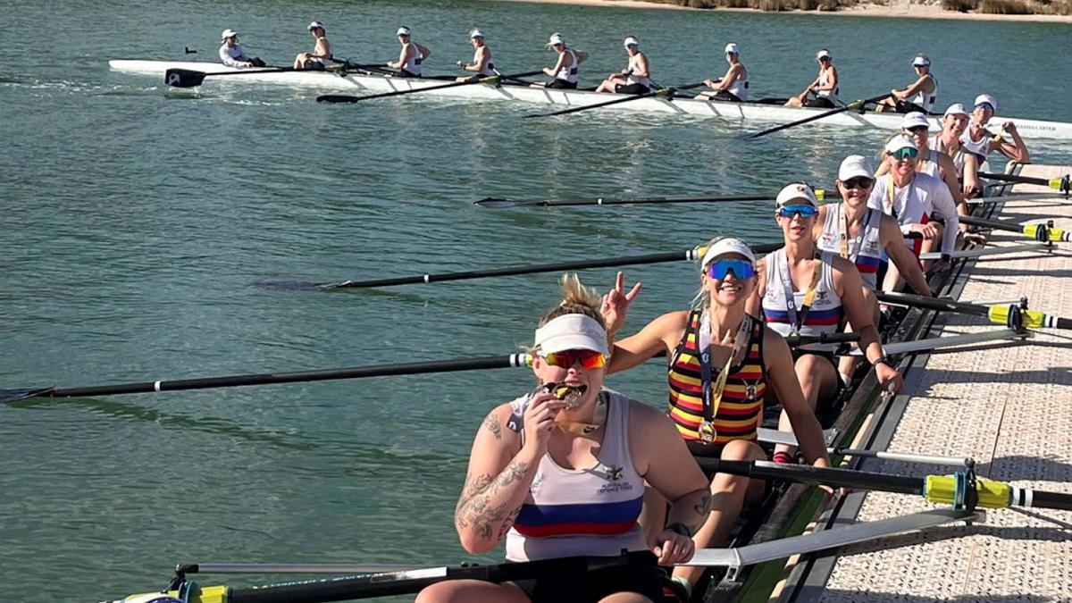 Two groups of women with medals sit in their row boats on a body of water.