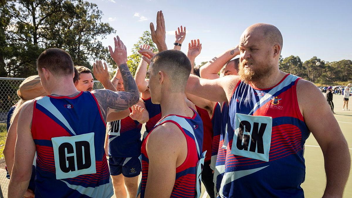 A team of male netball players perform a group high-five in a huddle