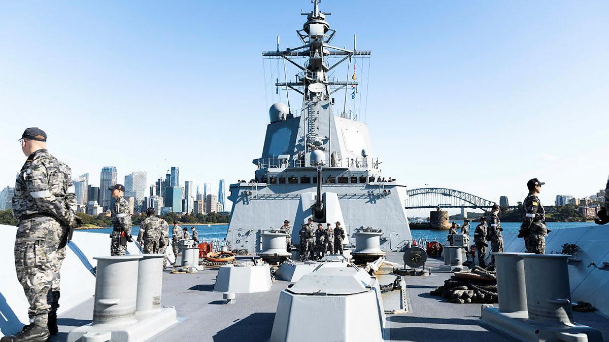 Sailors line the upper decks of a ship. 