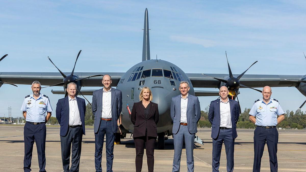 Seven people stand in a line in front of an aircraft on the tarmac.