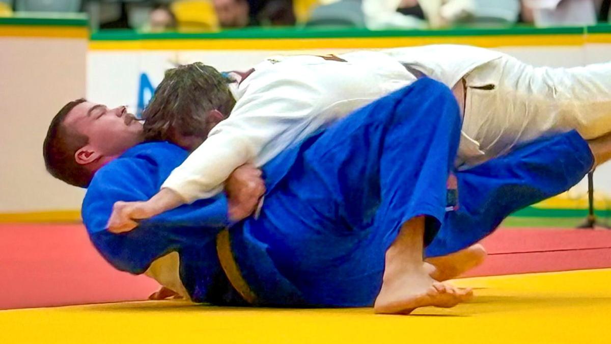 Two men, one in a blue judo uniform and one in a white judo uniform, wrestle during a competition.