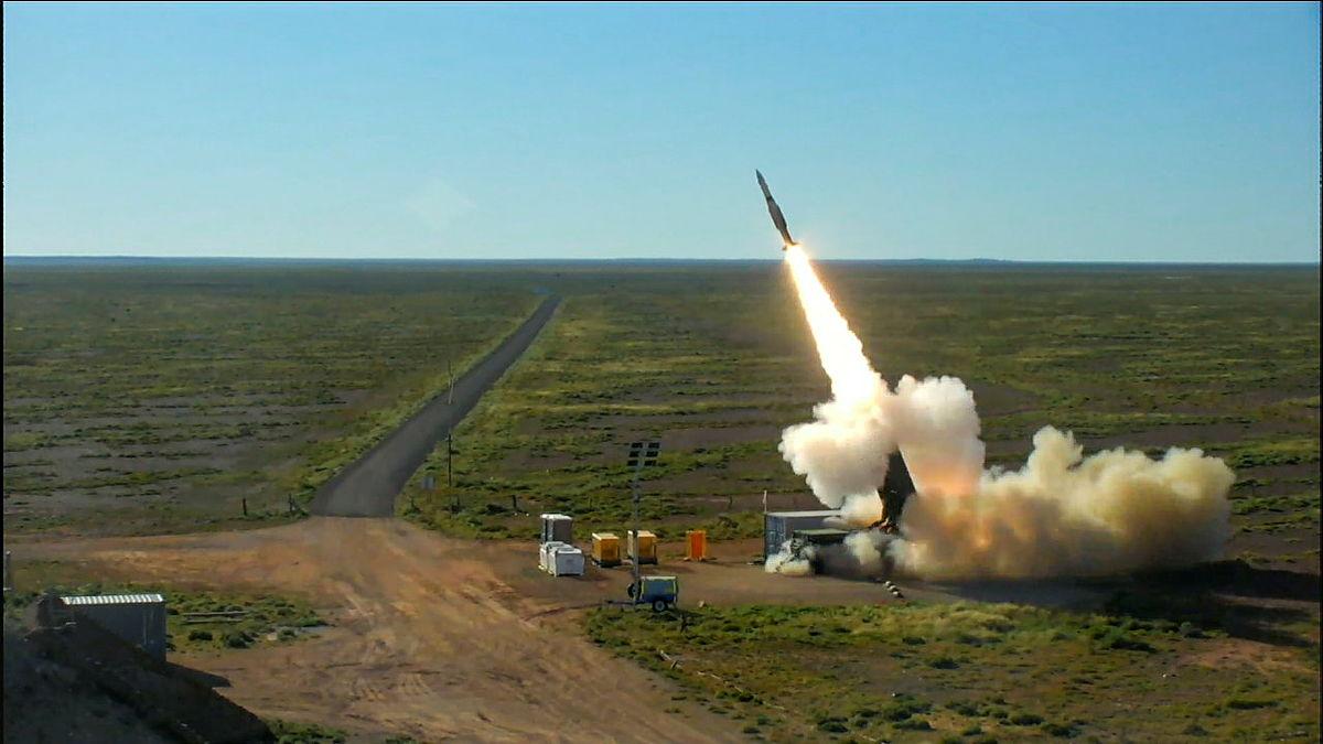 A missile is shot from a empty area of land into the sky.