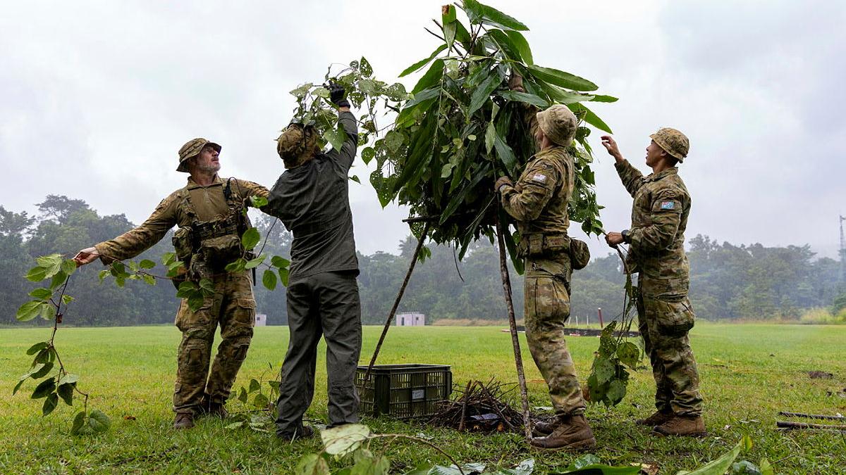 Four military personnel construct a triangle structure topped with leaves.