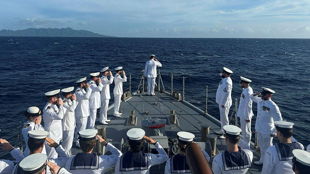 Sailors stand and salute on a boat at sea.