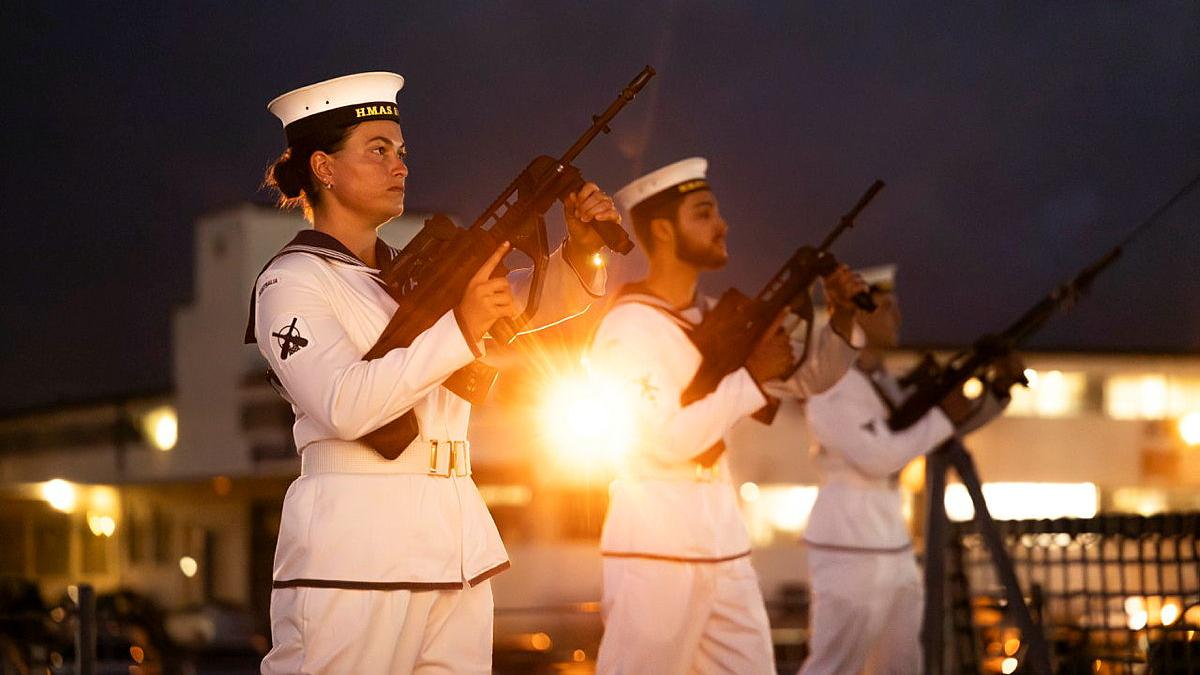 Three sailors stand in line and point guns in the air. 
