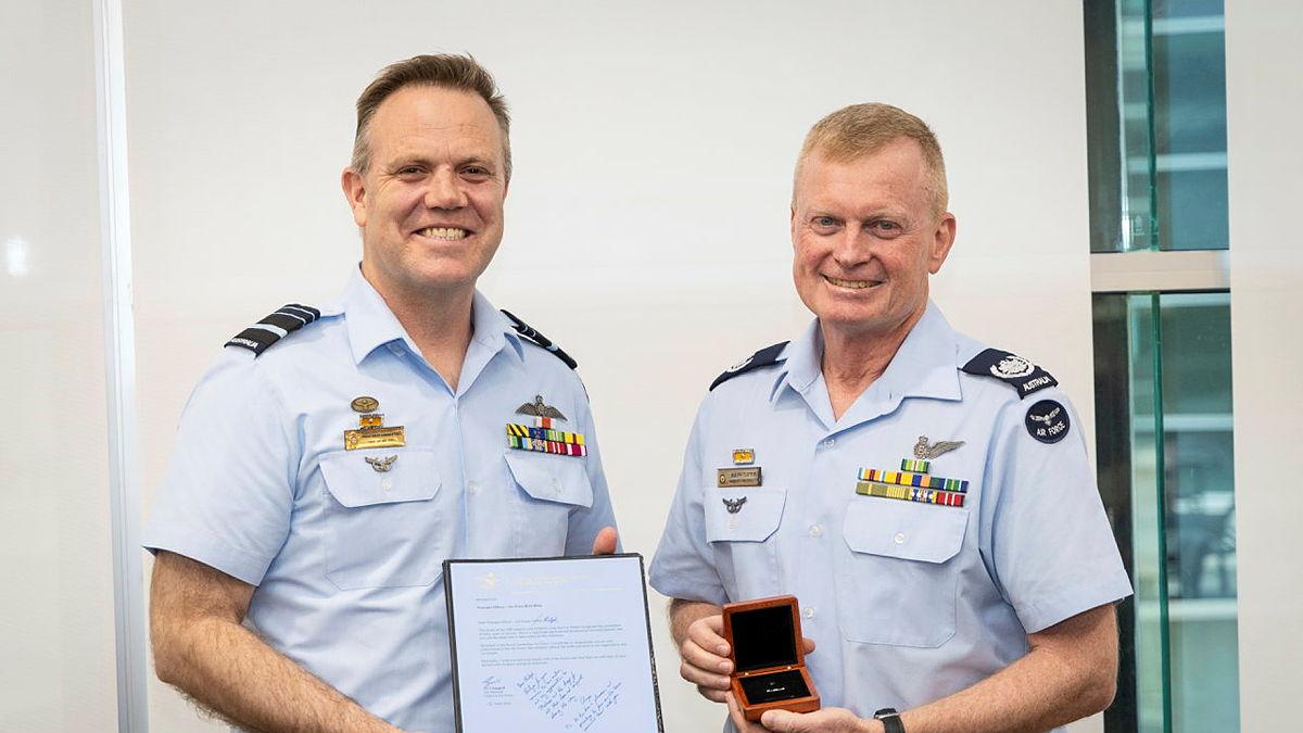 Two men in Air Force uniform stand holding awards and smiling at the camera.
