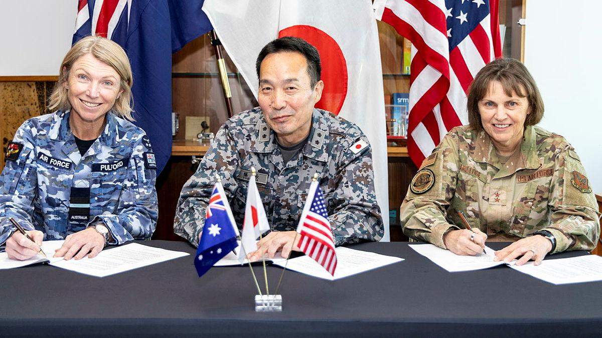 Three military personnel from Australia, Japan and the US all sign a document each.