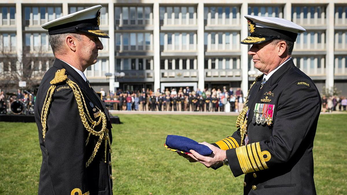 Two decorated military members exchange a folded piece of blue cloth.