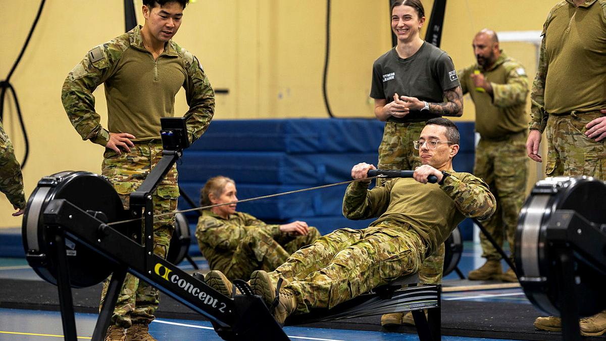 A group of military personnel watch another member use the rowing machine.