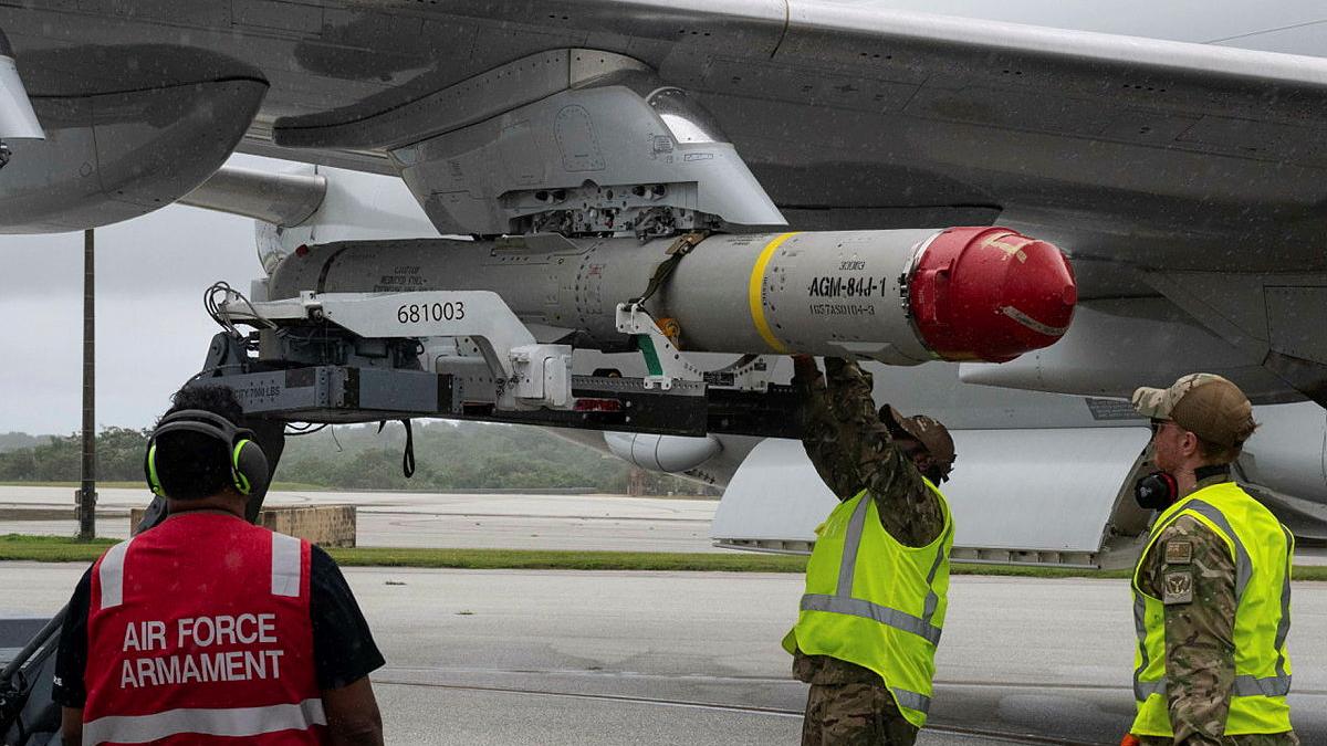 Military personnel load a missile onto an aircraft wing.