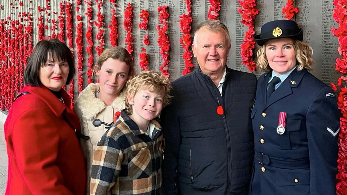 A group of people standing together in front on a memorial wall of poppies. 