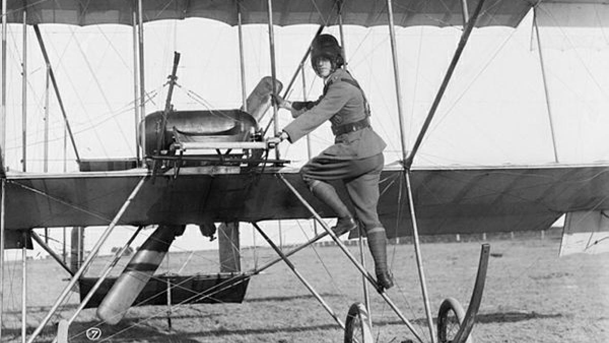 A black-and-white historical image of a man climbing into an aircraft.
