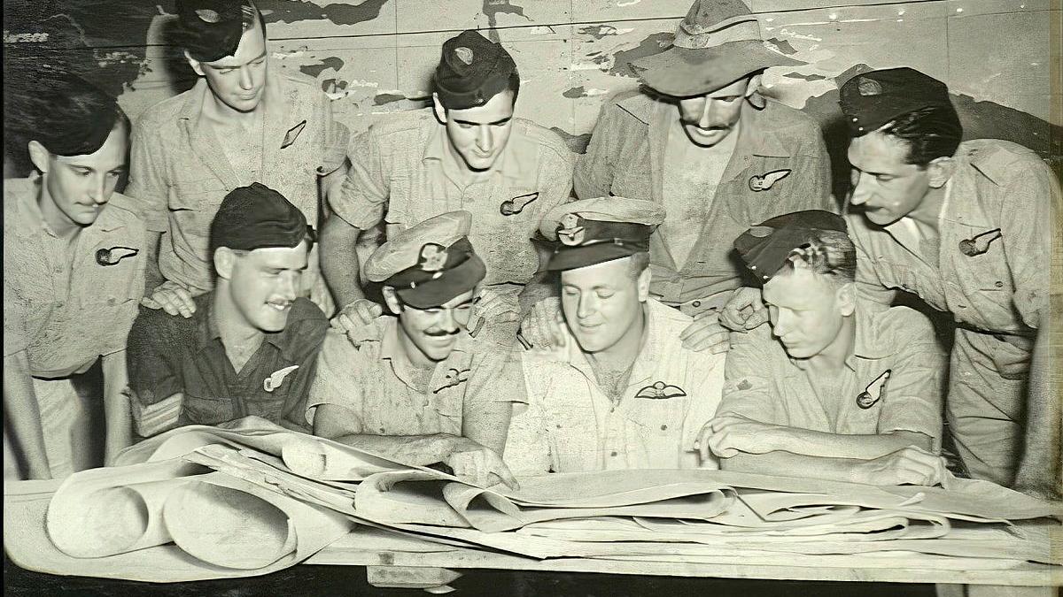 A black-and-white historical image of a group of men gathered around a table looking at maps.