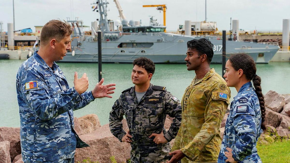 A man talks to three other people, all in military uniforms.