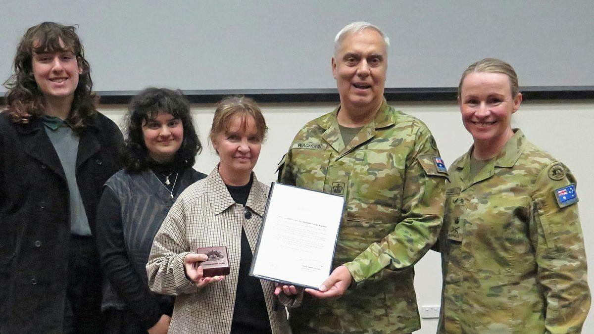A group of people pose with a certificate and a medal.