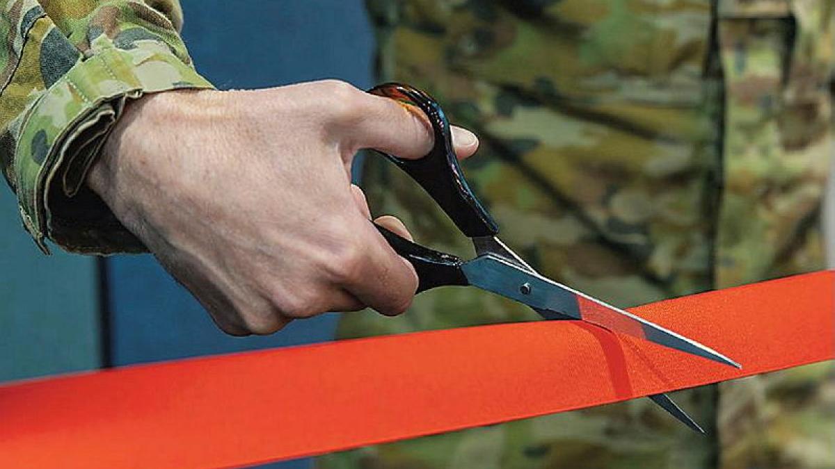 A soldier's hand holds scissors cutting a red tape.