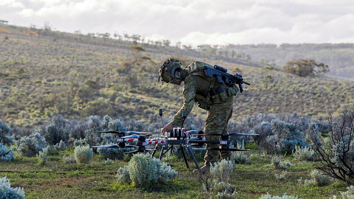 A soldier adjusts a large drone, positioned in an open field.