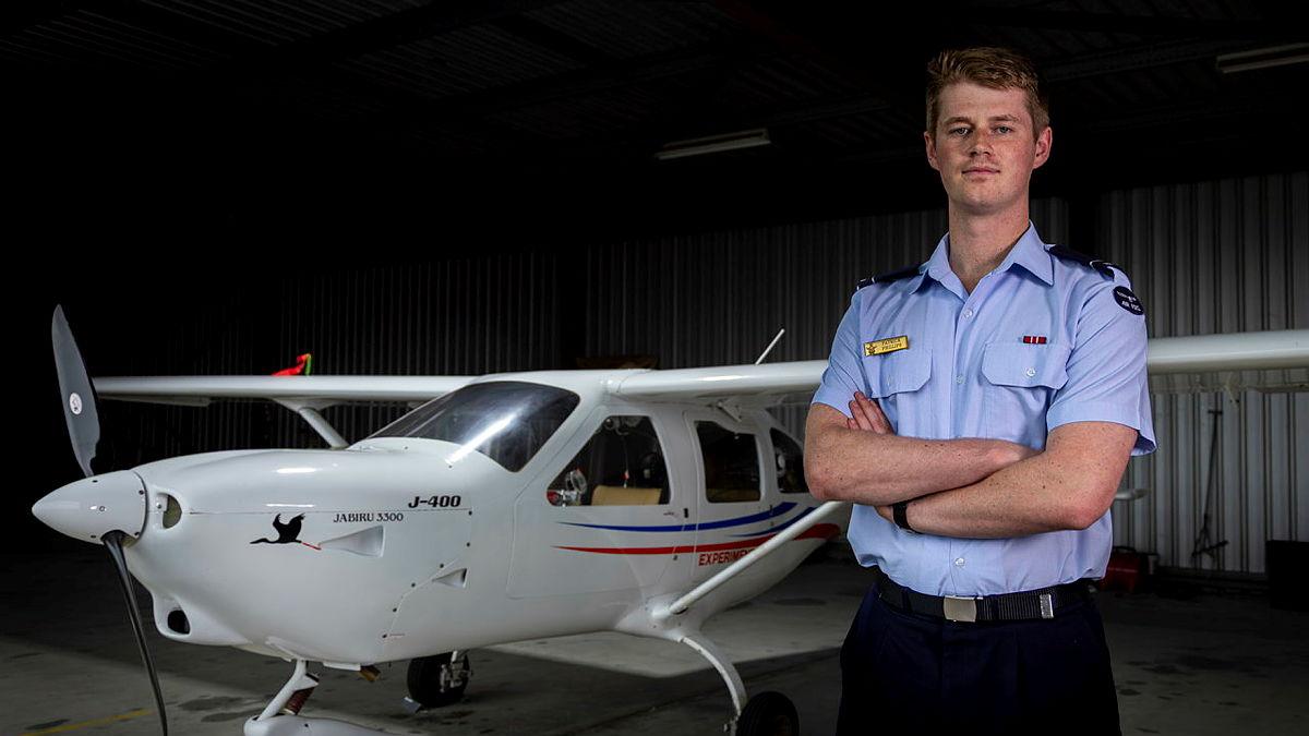 A man in uniform stands next to a small aircraft in a hangar.