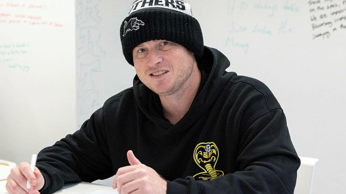 A man in a beanie and black jumper sitting at a table drawing.