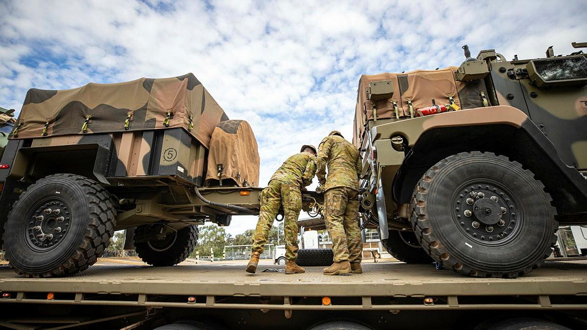 Two military members attach one military vehicle to another.
