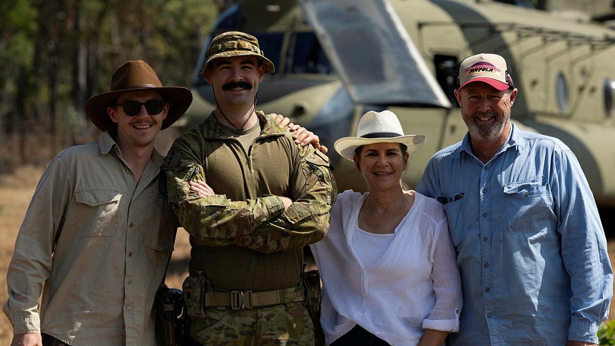 A man in uniform stands with three other people in casual clothes in front of an Army helicopter.
