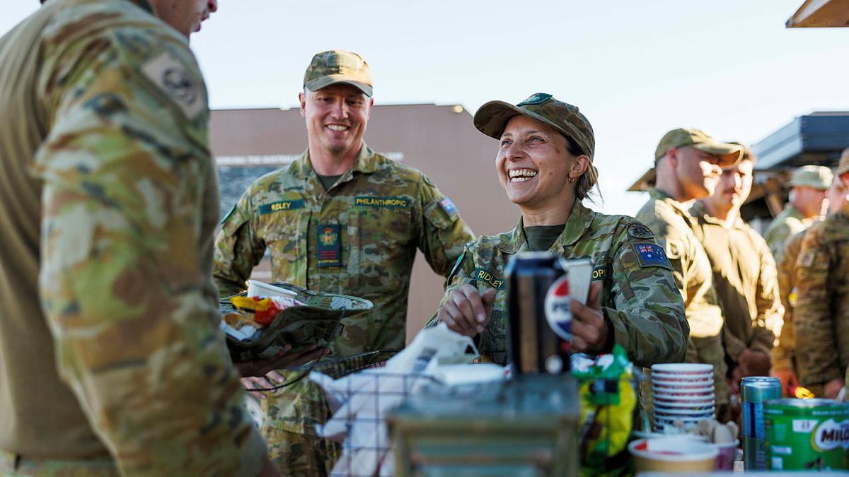 A military woman laughs as she talks to several other personnel.