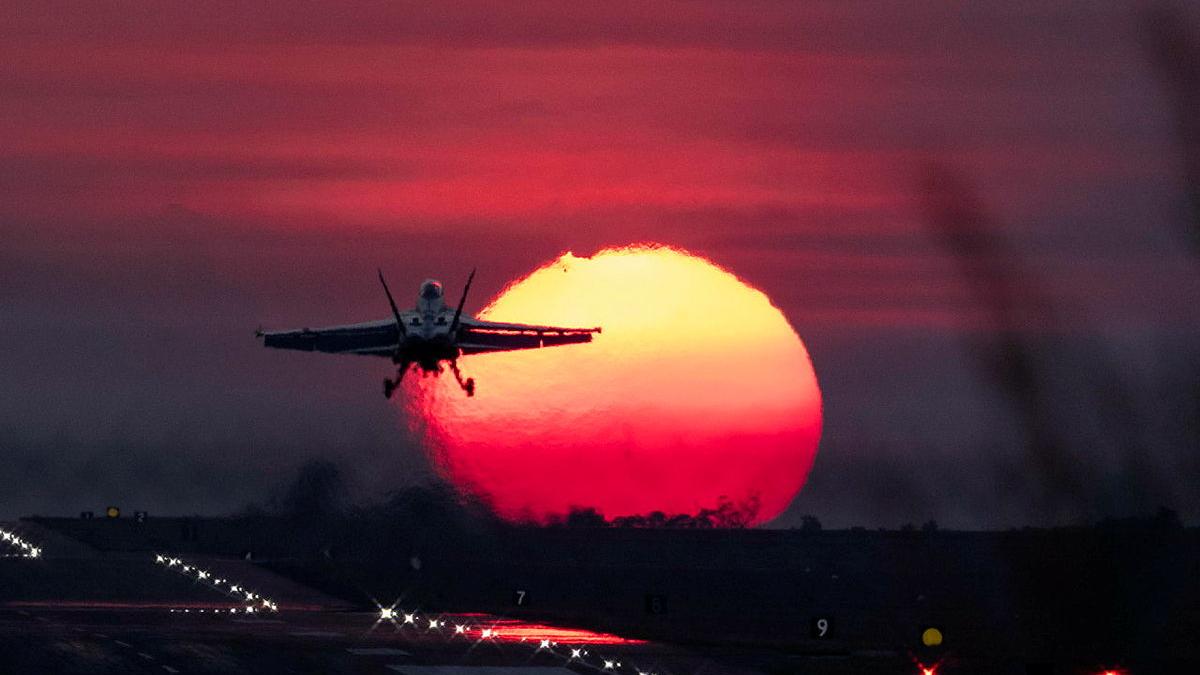 An aircraft flies off from the tarmac into the sunset.