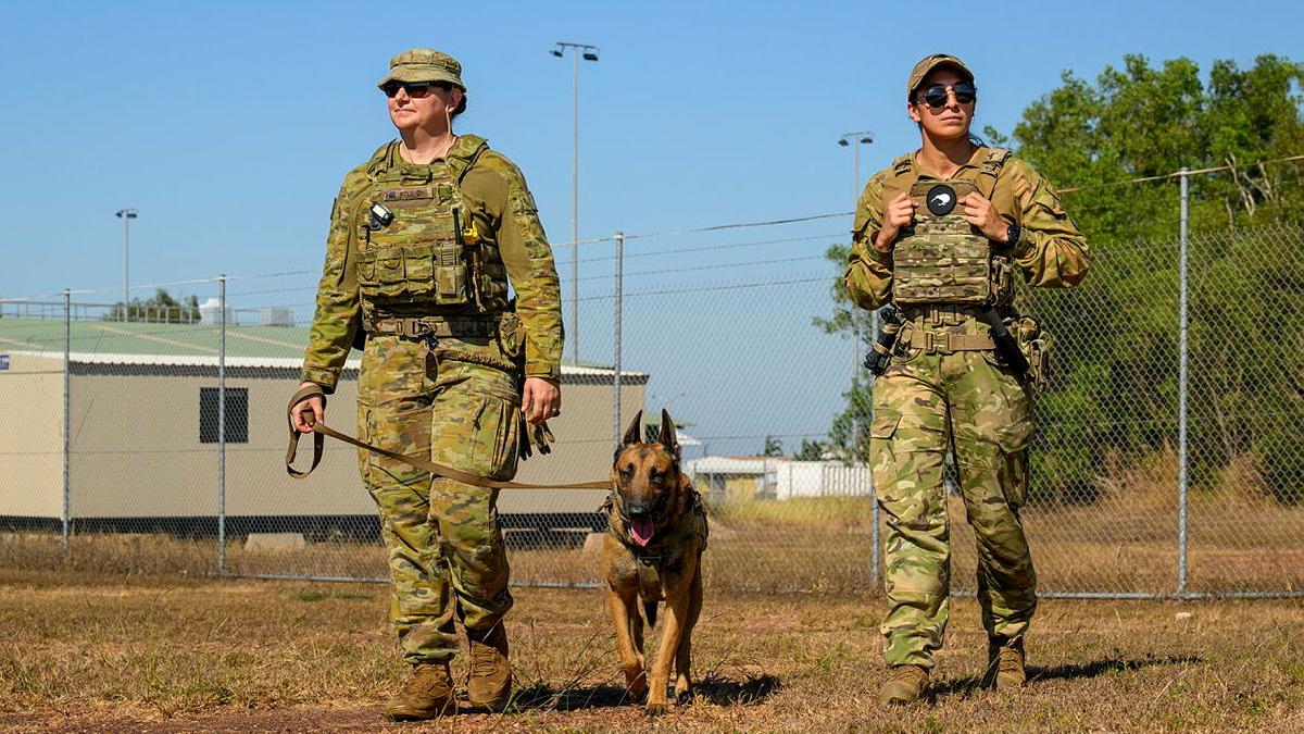 Two military women lead a working dog around a base.