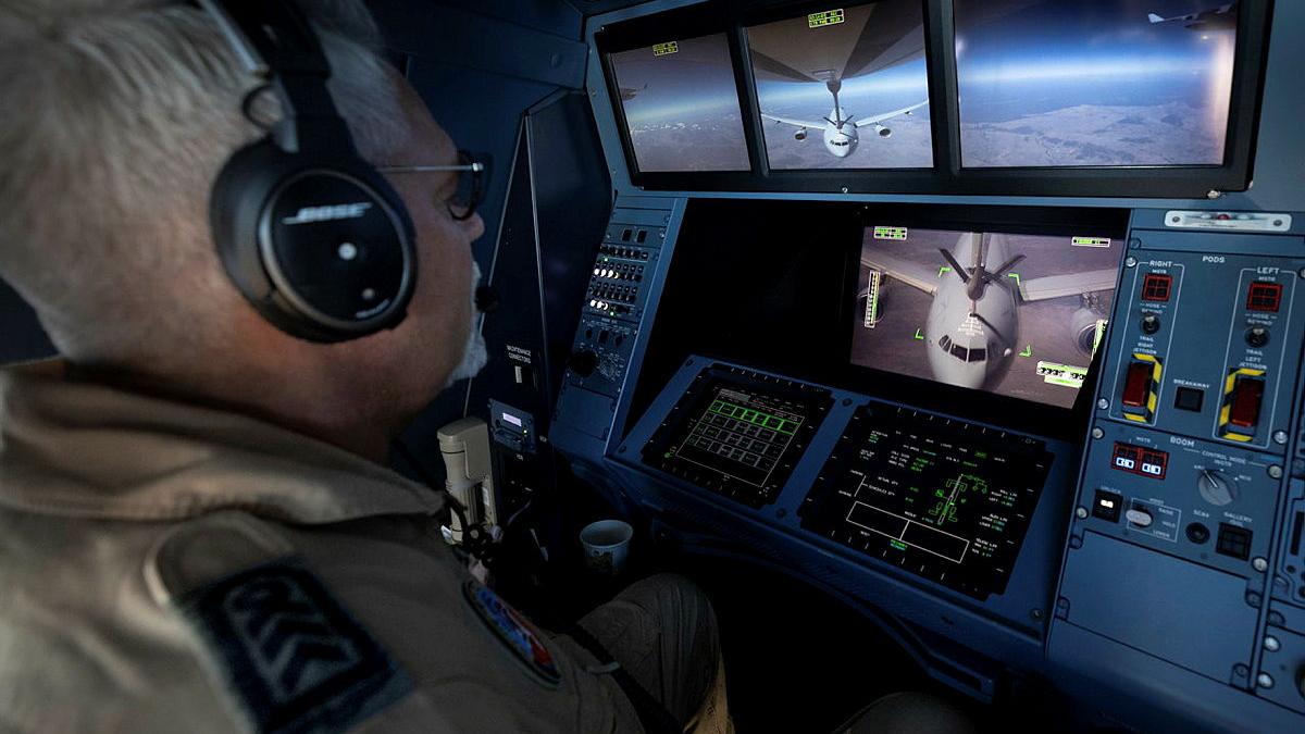 A military member looks at several screens of aircraft in flight.