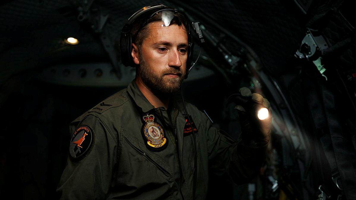 A military member searches in the dark of a cabin with a flashlight.