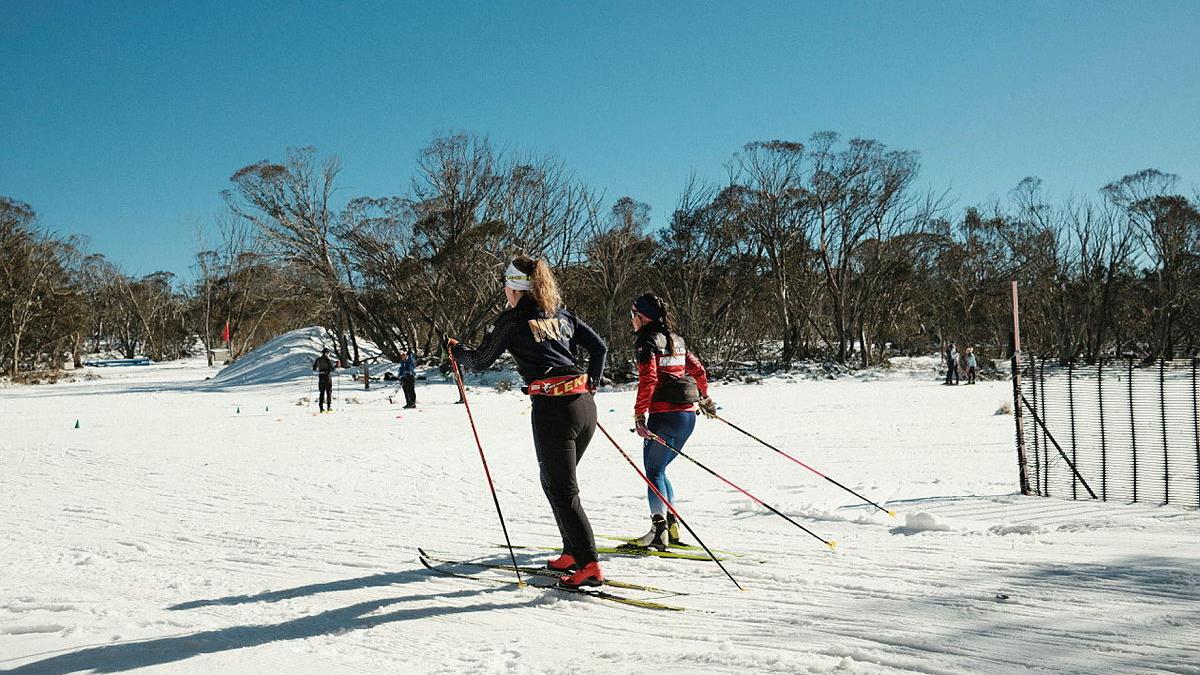 Two female skiiers move side-by-side on flat, snowy ground.
