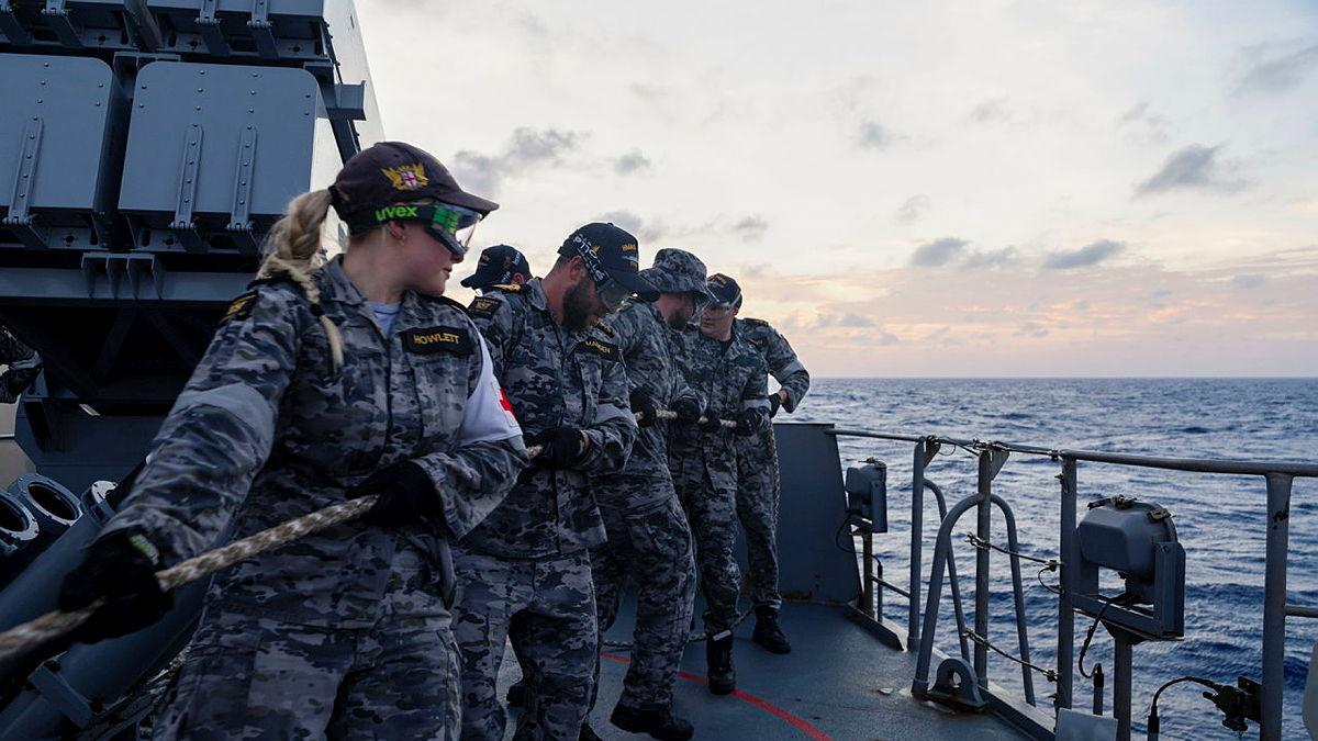 A small group of sailors all pull on a rope on board a ship.